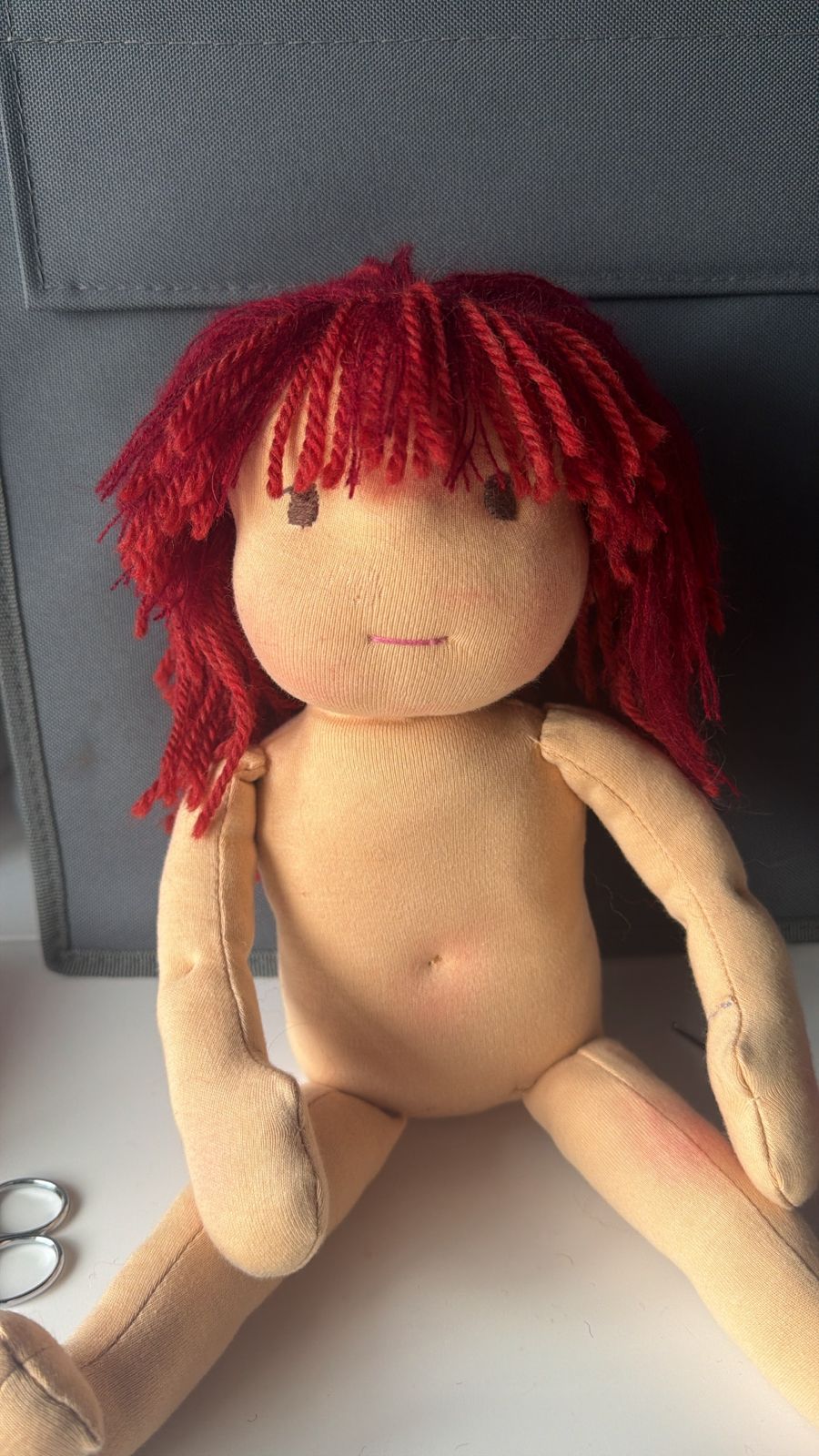 Una muñeca todavía sin vestir: cuerpo de tela, cara bordada y pelo rojo.