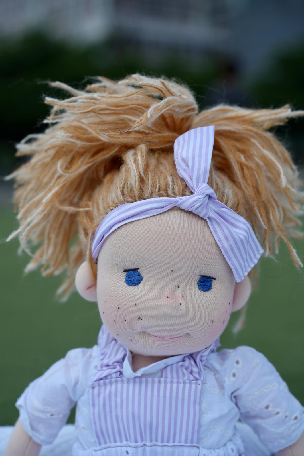 Primer plano de la muñeca del moño lila: ojos azules bordados y pecas.
