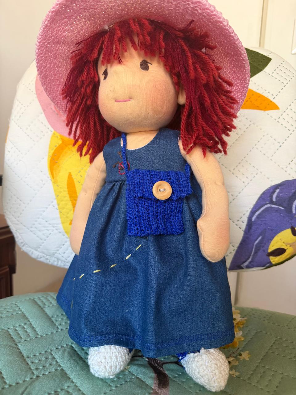 La misma muñeca con sombrero rosado y su bolsito azul de crochet con botón de madera.